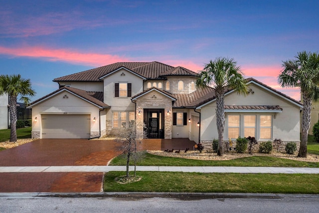 mediterranean / spanish-style home with aphalt driveway, a garage, stone siding, a tiled roof, and stucco siding