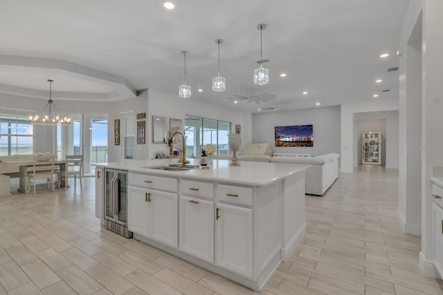 kitchen with ceiling fan with notable chandelier, sink, a center island with sink, white cabinetry, and hanging light fixtures