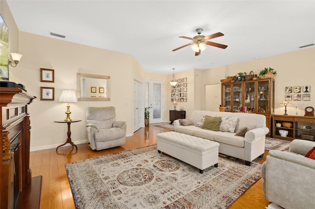 living room featuring a ceiling fan, wood finished floors, visible vents, and baseboards