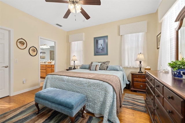 bedroom featuring visible vents, a ceiling fan, ensuite bath, wood finished floors, and baseboards