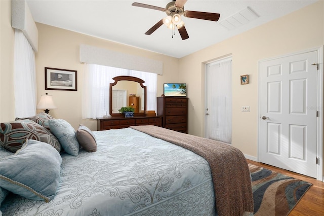 bedroom with baseboards, ceiling fan, visible vents, and wood finished floors