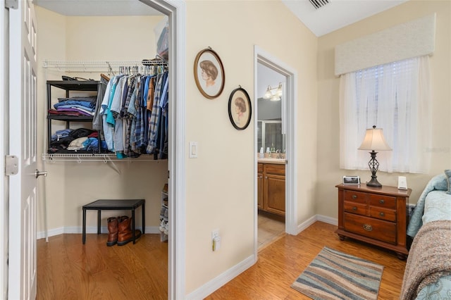 bedroom featuring visible vents, baseboards, a closet, light wood finished floors, and ensuite bath