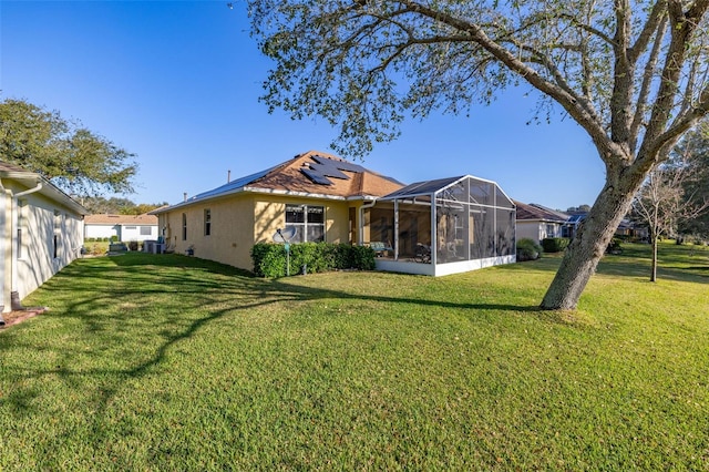 back of house with a sunroom, a yard, solar panels, and stucco siding