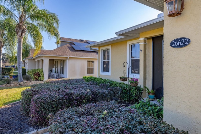 view of front of house featuring a shingled roof, solar panels, and stucco siding