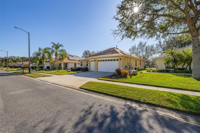 single story home with driveway, a garage, a front yard, roof mounted solar panels, and stucco siding