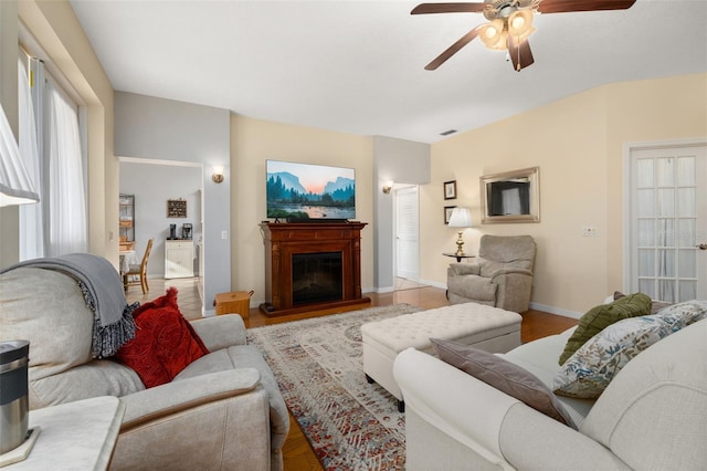 living room featuring light wood finished floors, visible vents, baseboards, a glass covered fireplace, and ceiling fan