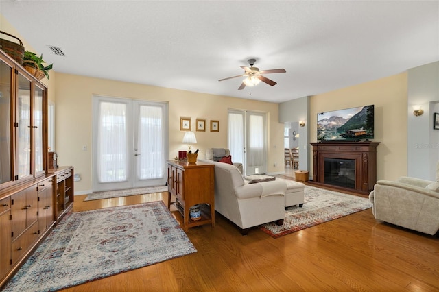 living room with visible vents, a glass covered fireplace, wood finished floors, and french doors