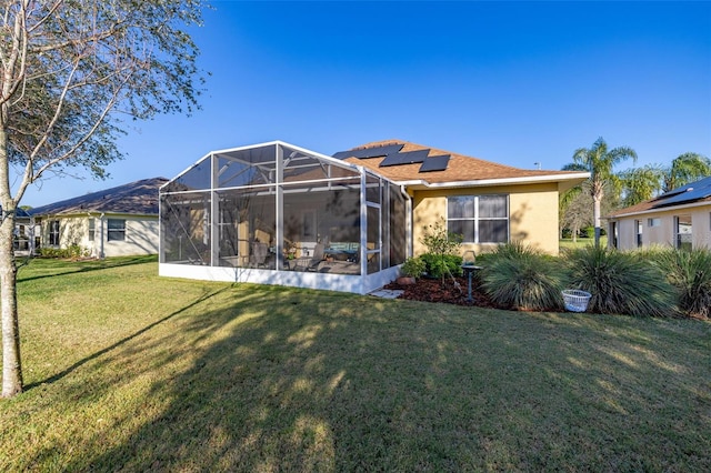 rear view of house featuring solar panels, a lawn, and stucco siding