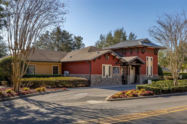 view of front of house with metal roof, stone siding, driveway, stucco siding, and a standing seam roof