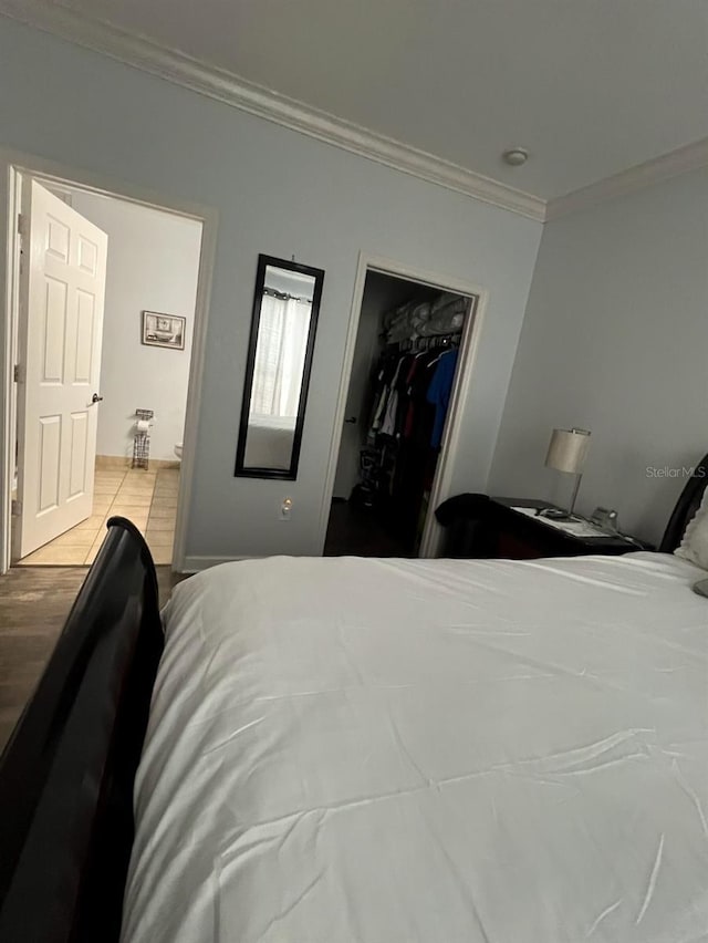 bedroom with a spacious closet, light wood-type flooring, ornamental molding, and a closet