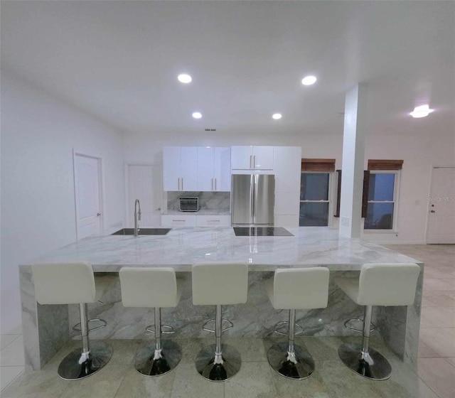 kitchen with a kitchen breakfast bar, light stone counters, sink, white cabinets, and stainless steel refrigerator