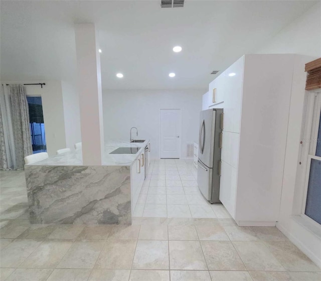 kitchen with stainless steel refrigerator, white cabinetry, sink, light stone countertops, and light tile patterned flooring