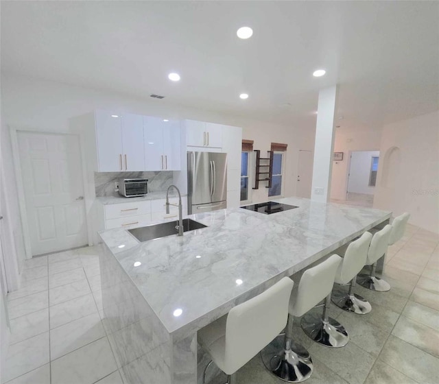 kitchen featuring stainless steel refrigerator, white cabinetry, sink, light stone counters, and a breakfast bar