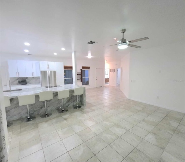 kitchen featuring decorative backsplash, a kitchen breakfast bar, light tile patterned floors, white cabinetry, and stainless steel refrigerator