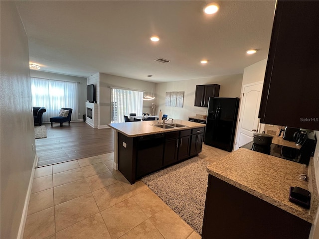 kitchen featuring stove, sink, light tile patterned flooring, an island with sink, and black refrigerator