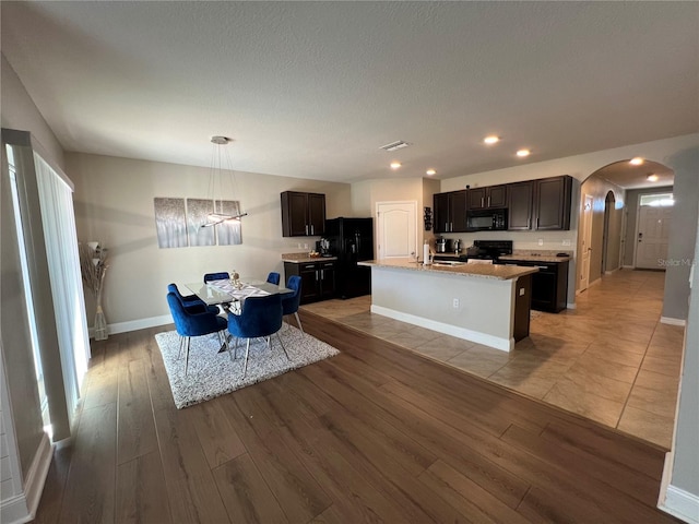 kitchen with light hardwood / wood-style floors, hanging light fixtures, black appliances, and a center island with sink