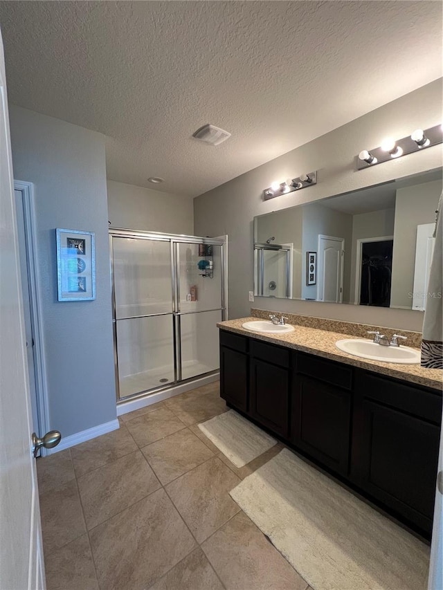 bathroom featuring a shower with shower door, vanity, tile patterned floors, and a textured ceiling