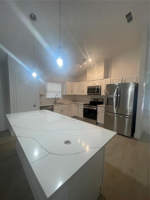 kitchen featuring pendant lighting, lofted ceiling, light stone countertops, appliances with stainless steel finishes, and white cabinetry