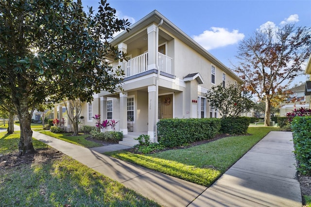 view of front of house featuring stucco siding, a balcony, a porch, and a front lawn