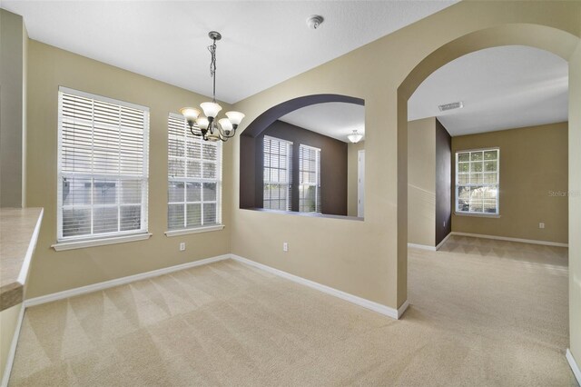 carpeted spare room featuring visible vents, baseboards, a notable chandelier, and plenty of natural light