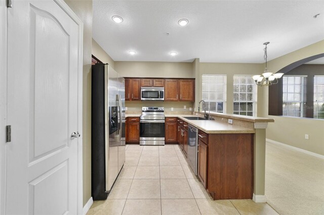 kitchen featuring light countertops, light tile patterned floors, appliances with stainless steel finishes, a peninsula, and a sink