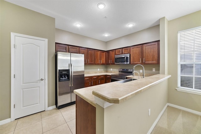 kitchen featuring a sink, appliances with stainless steel finishes, a peninsula, light tile patterned flooring, and light countertops