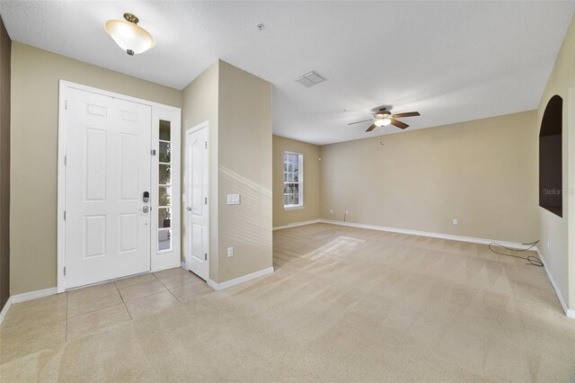 foyer entrance featuring light tile patterned floors, baseboards, visible vents, ceiling fan, and light carpet