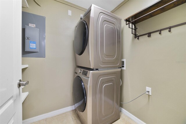 laundry room featuring baseboards, stacked washing maching and dryer, laundry area, electric panel, and tile patterned flooring