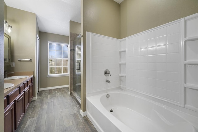 bathroom featuring wood finished floors, a shower with shower door, double vanity, a sink, and a bath