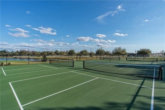 view of tennis court featuring fence and a water view