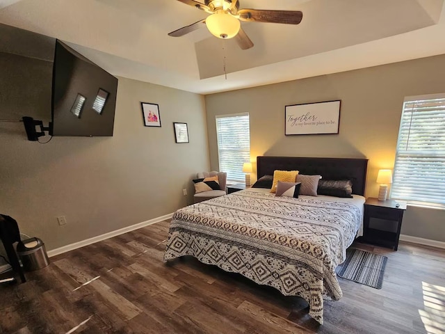 bedroom featuring hardwood / wood-style floors, ceiling fan, a raised ceiling, and multiple windows