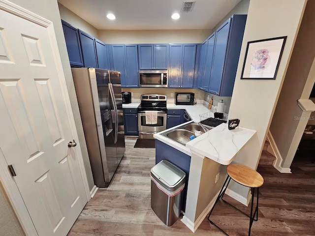 kitchen featuring a kitchen breakfast bar, sink, blue cabinetry, appliances with stainless steel finishes, and kitchen peninsula