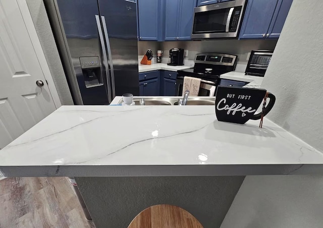 kitchen featuring light hardwood / wood-style flooring, light stone countertops, blue cabinetry, appliances with stainless steel finishes, and kitchen peninsula