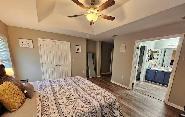 bedroom with ceiling fan, ensuite bathroom, hardwood / wood-style floors, a tray ceiling, and a closet