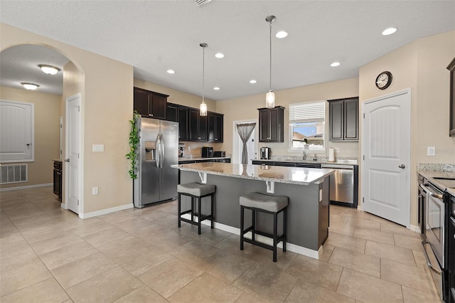 kitchen featuring light stone counters, hanging light fixtures, appliances with stainless steel finishes, and a kitchen island