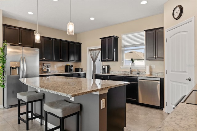 kitchen featuring light stone countertops, appliances with stainless steel finishes, a kitchen island, sink, and hanging light fixtures