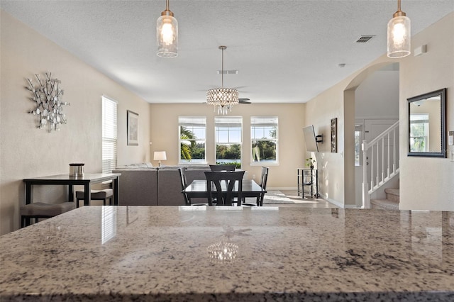 kitchen with light stone countertops, a textured ceiling, a chandelier, and hanging light fixtures