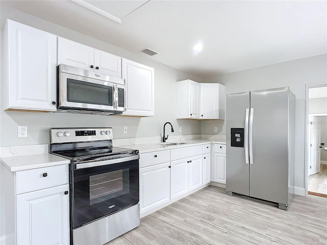 kitchen with stainless steel appliances, light hardwood / wood-style floors, white cabinets, and sink