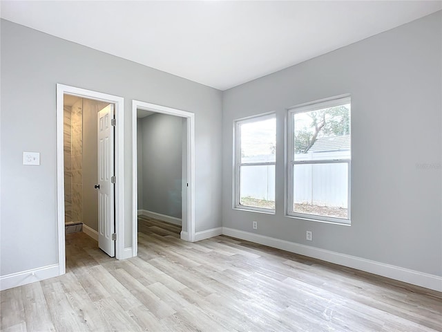 unfurnished bedroom with light hardwood / wood-style floors, a spacious closet, connected bathroom, and multiple windows