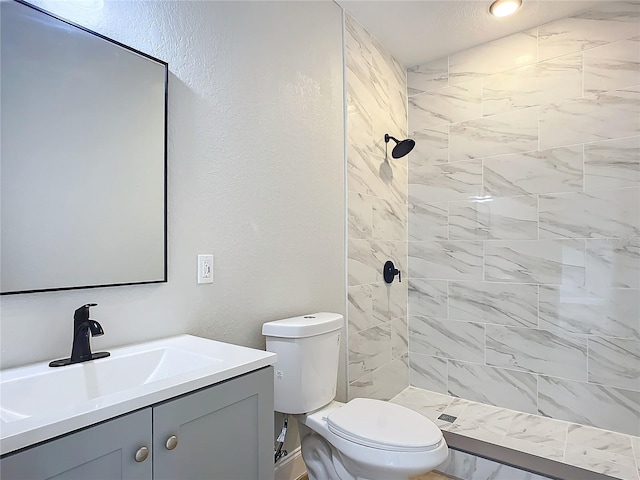 bathroom with toilet, tiled shower, and vanity