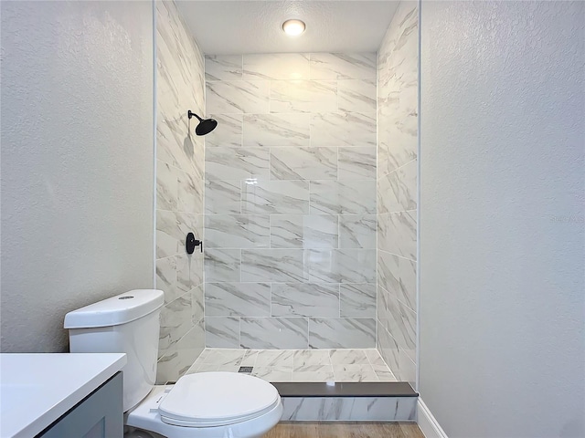 bathroom with hardwood / wood-style floors, tiled shower, vanity, and toilet