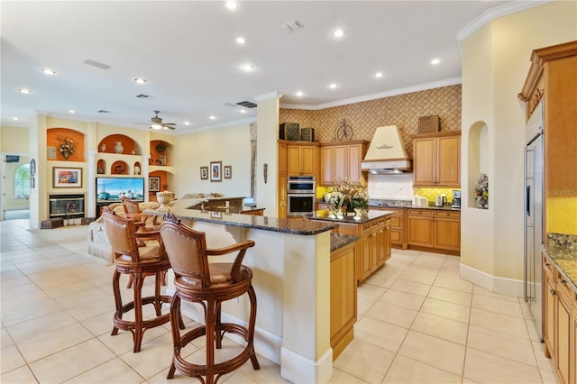 kitchen with a large island, dark stone countertops, a breakfast bar area, premium range hood, and ceiling fan