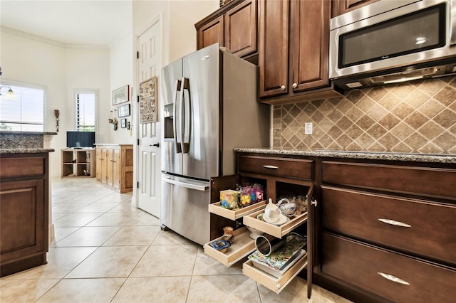 kitchen with crown molding, dark stone countertops, light tile patterned floors, appliances with stainless steel finishes, and tasteful backsplash