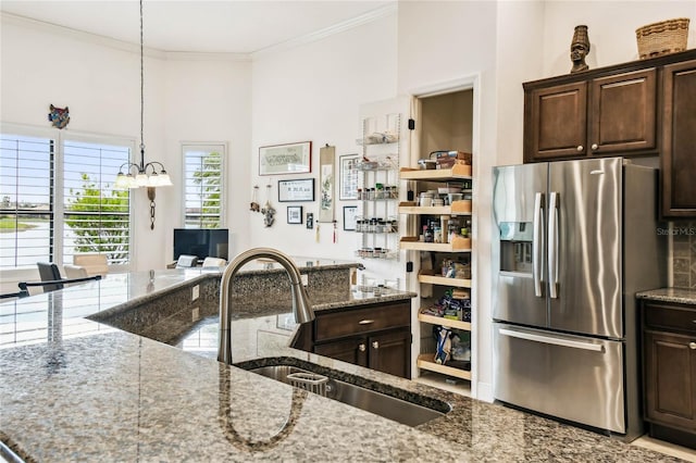 kitchen featuring stainless steel fridge, light stone counters, dark brown cabinets, and sink