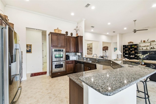 kitchen featuring ceiling fan, sink, stainless steel appliances, dark stone countertops, and a breakfast bar