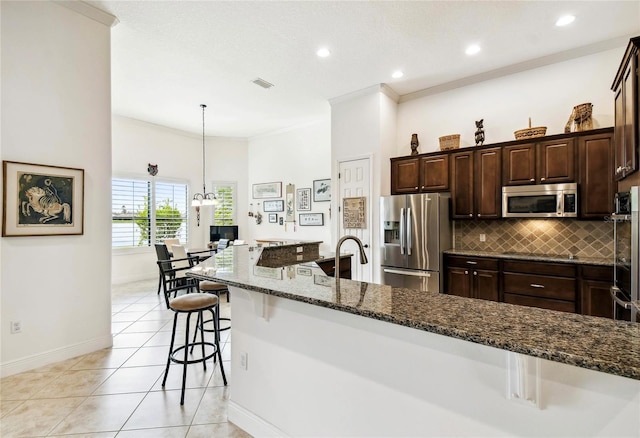 kitchen featuring stainless steel appliances, backsplash, dark stone countertops, decorative light fixtures, and a breakfast bar