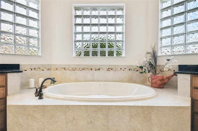 bathroom with vanity, a healthy amount of sunlight, and tiled tub