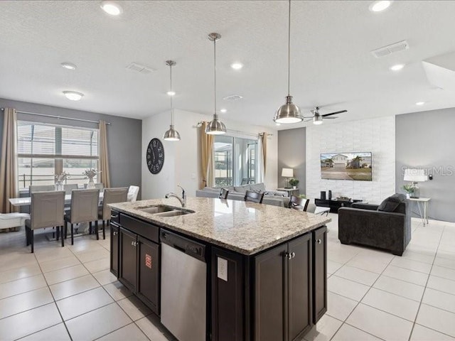 kitchen featuring sink, decorative light fixtures, a center island with sink, stainless steel dishwasher, and light stone countertops