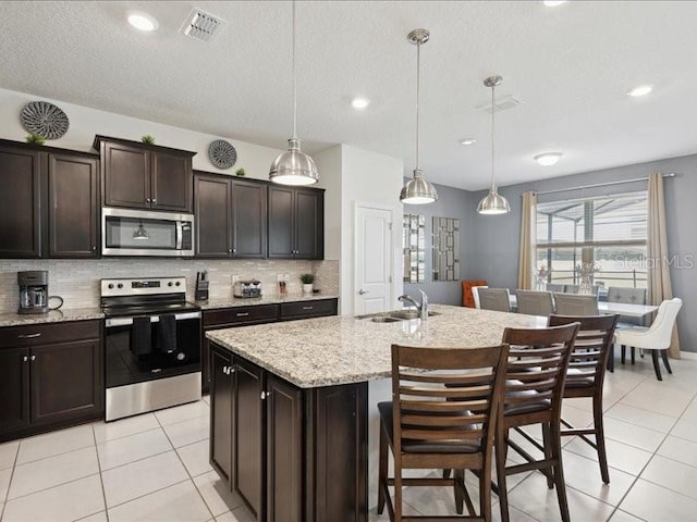 kitchen featuring appliances with stainless steel finishes, decorative light fixtures, sink, a kitchen island with sink, and dark brown cabinets