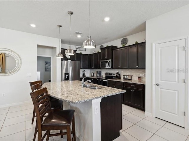 kitchen with appliances with stainless steel finishes, pendant lighting, sink, a kitchen bar, and a center island with sink